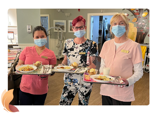 3 smiling Red Deer Hospice staff members holding trays with dinner to deliver.