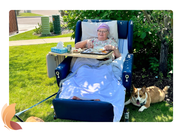 Resident enjoying the sunny outdoors while eating lunch. Her 2 dogs are nearby.