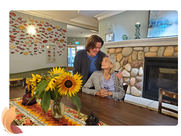 Red Deer Hospice staff member with her arm around a woman in the dining room of the Red Deer Hospice. Fireplace in the foreground.