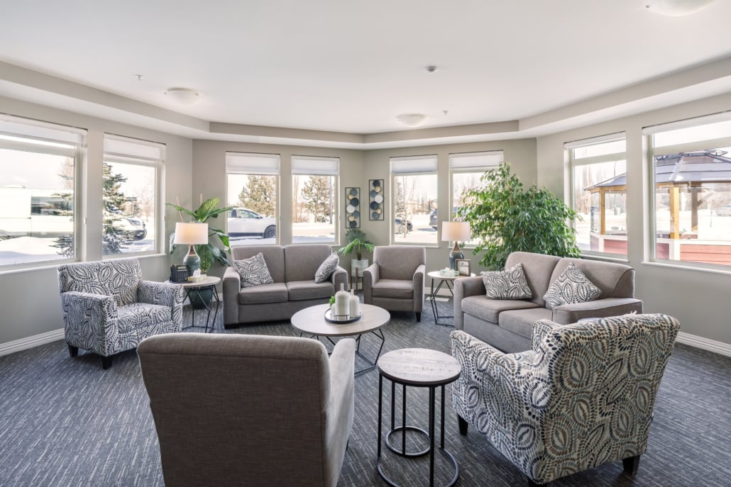 Room with lots of windows, plants and multiple cozy couches and armchairs for sitting.