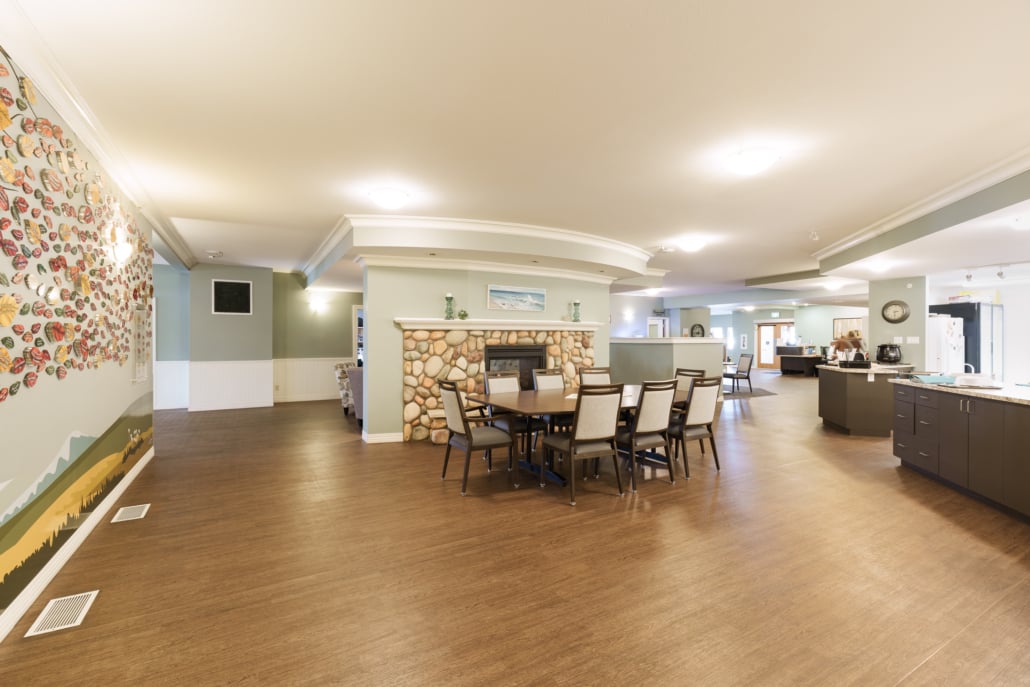 Large dining room table and chairs in front of fireplace with kitchen on the side.